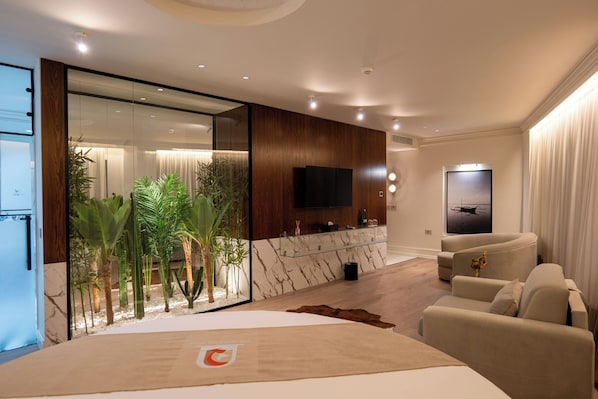 A modern hotel room with a large bed, a seating area with a sofa, a TV mounted on the wall, and a large window with curtains. - The Collector hotel boutique (Sarandë)