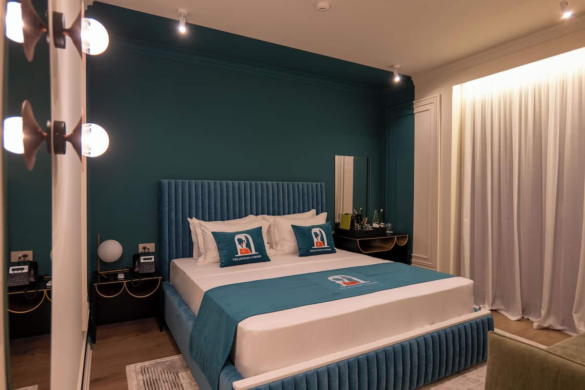 A modern bedroom with a large bed, teal walls, and a white headboard.