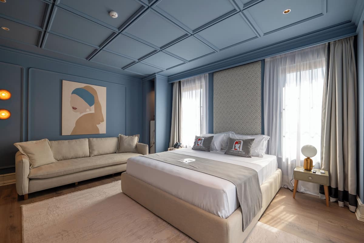 A bedroom with a large bed, a sofa, a nightstand, and a painting on the wall.