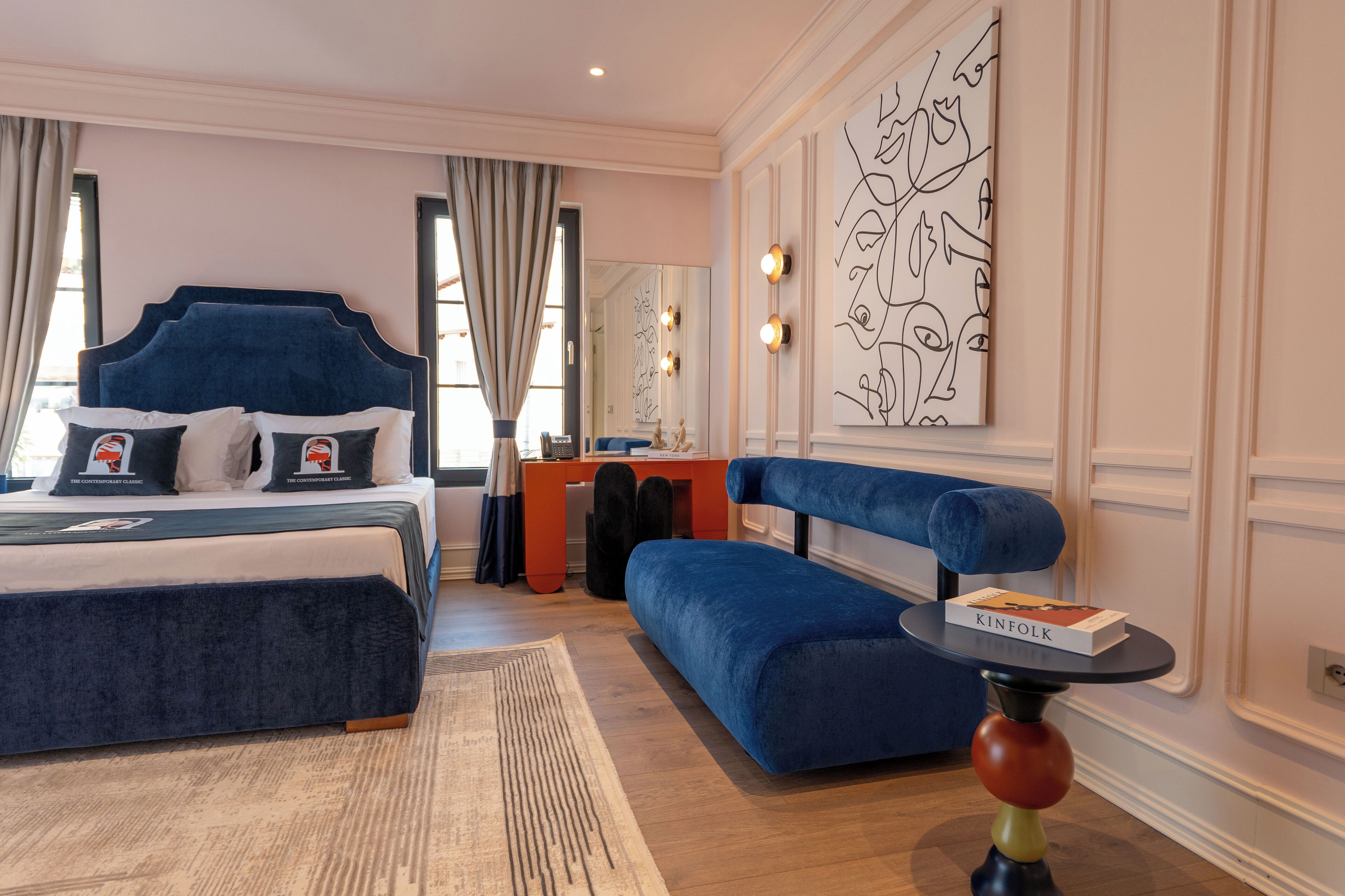 A modern hotel room with a large bed, a blue sofa, a desk, and a large abstract painting on the wall.