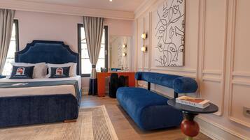 A modern hotel room with a large bed, a blue sofa, a desk, and a large abstract painting on the wall.