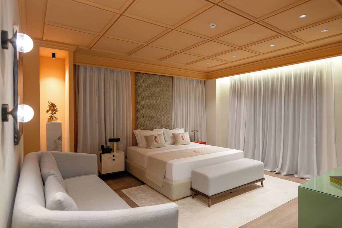 A modern hotel room with a large bed, a sofa, a nightstand, and a desk.