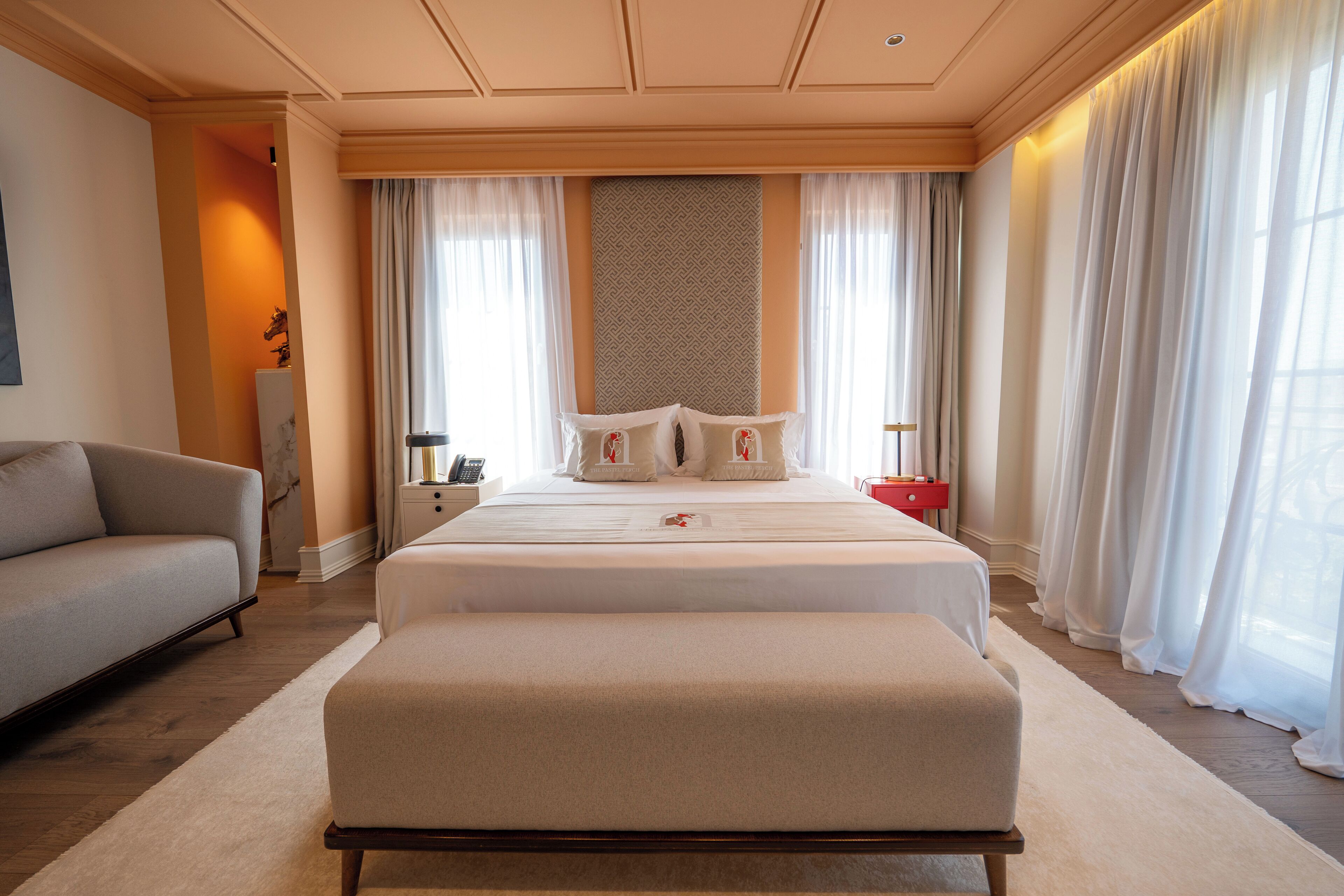 A hotel room with a large bed, a sofa, a bedside table with a lamp, and a nightstand with a phone.