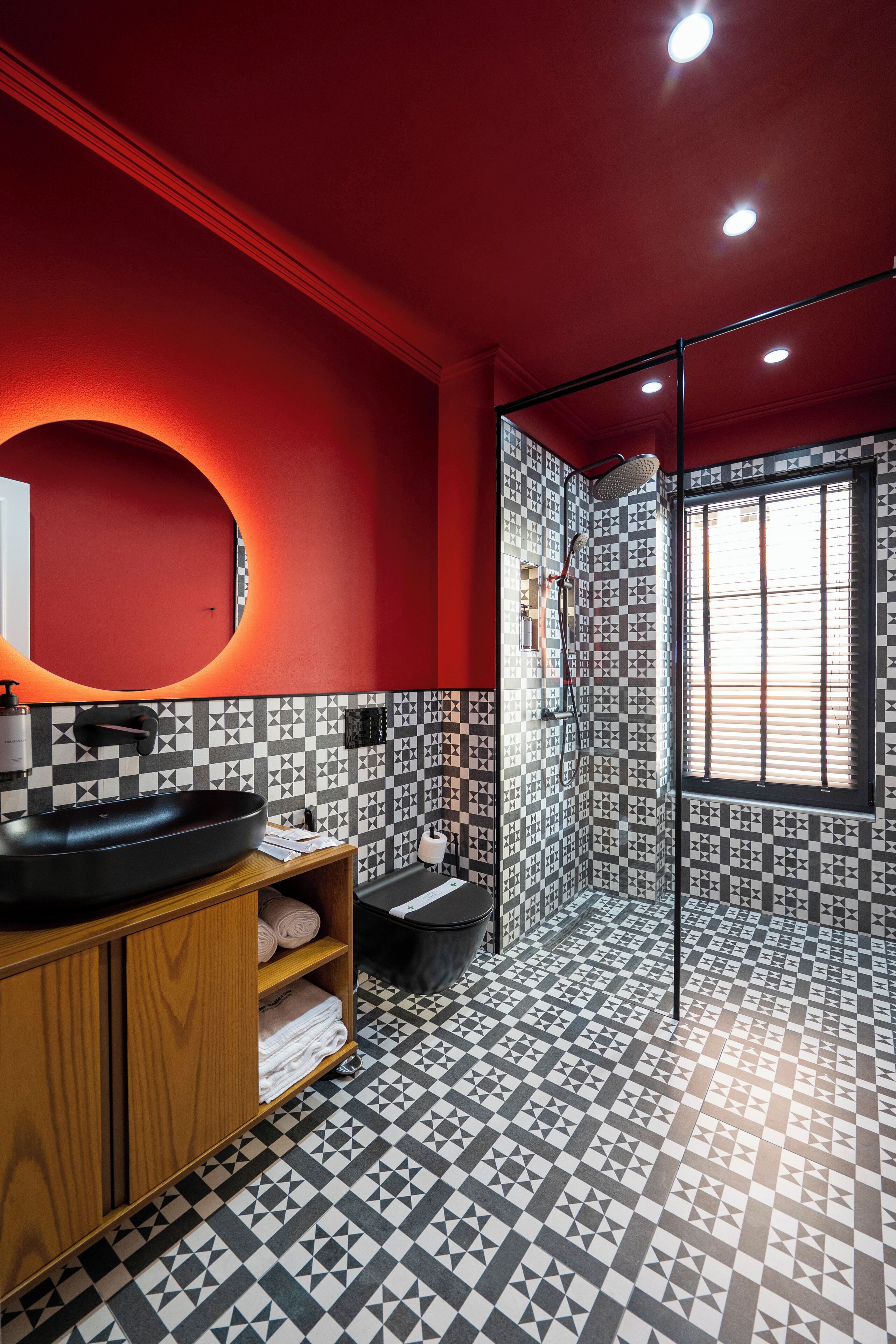 A modern bathroom with a black and white checkered floor, a red accent wall, and a large mirror.