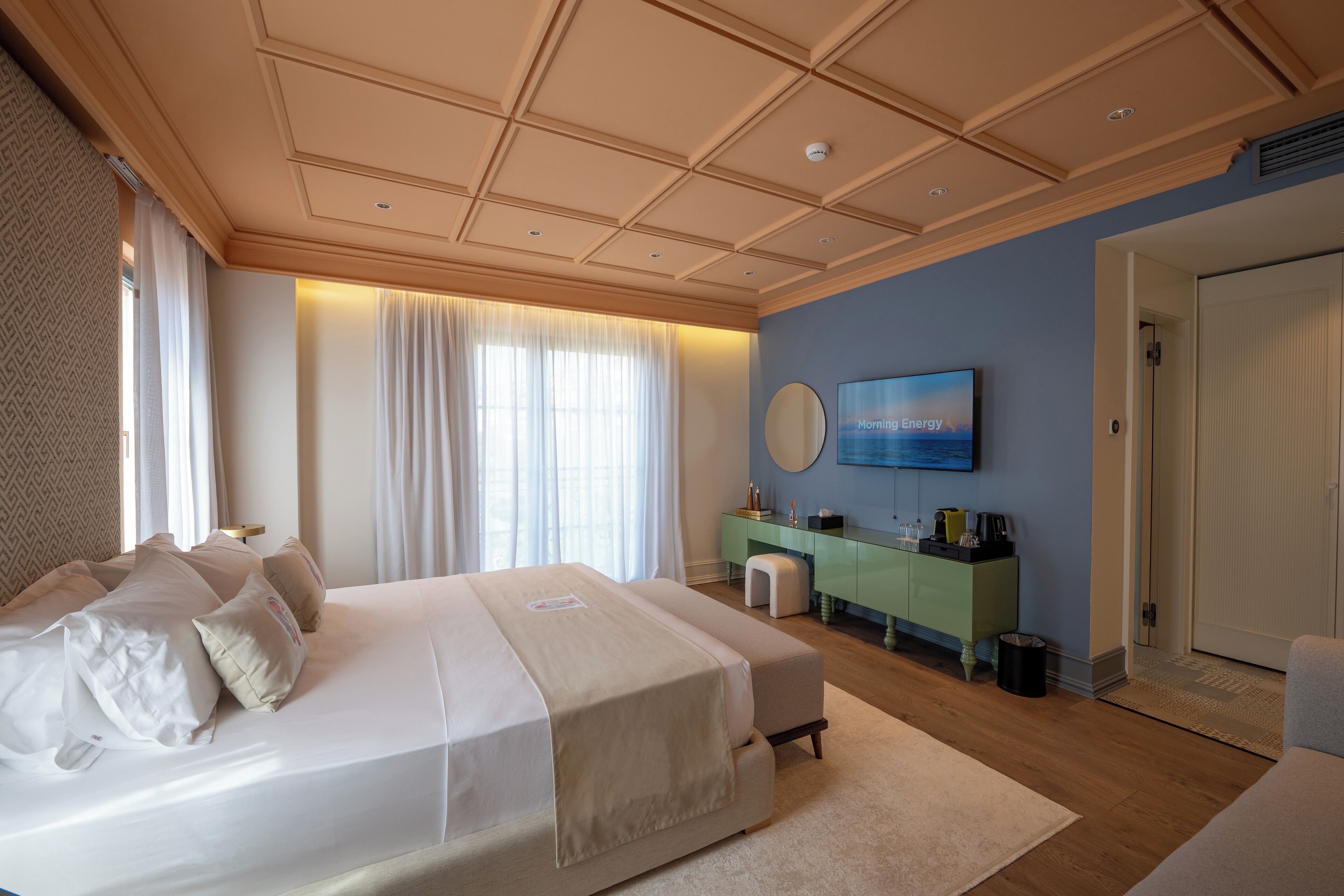A modern bedroom with a large bed, a green vanity, and a flat-screen TV on the wall.