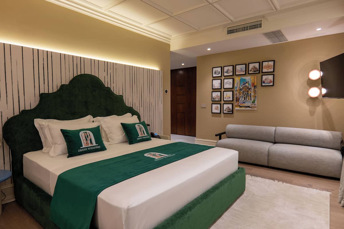 A hotel room with a large bed, a sofa, and a wall with framed pictures.