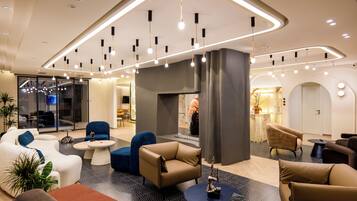 A modern hotel lobby with seating areas, a fireplace, and contemporary lighting fixtures.
