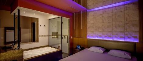 Una habitación de hotel moderna con una cama grande, un baño independiente con ducha de vidrio y un diseño de pared único.