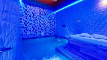 A blue-lit indoor pool area with geometric wall patterns and a seating area with steps leading into the water.