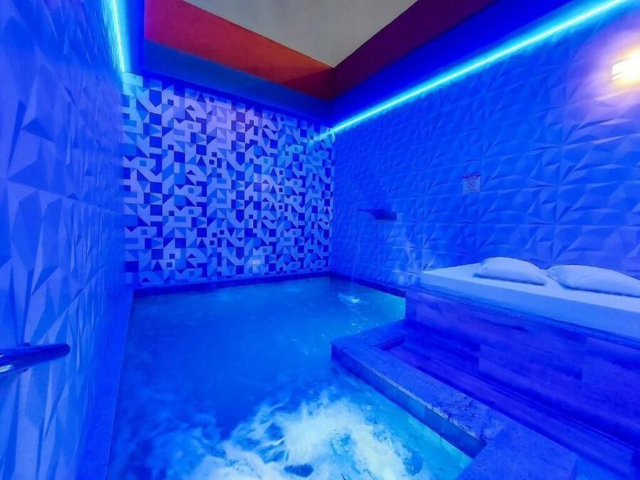 A blue-lit indoor pool area with geometric wall patterns and a seating area with steps leading into the water.