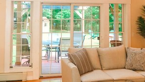 A spacious living room with a high ceiling, a large window, and a sliding glass door leading to an outdoor area. - Large Cozy Home •Songo River•Brandy Pond•Long Lake•Sebago (Naples)