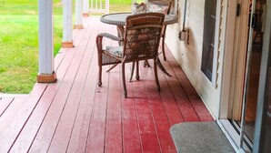 A covered porch with a red wooden floor, a round table, and wicker chairs. - Large Cozy Home •Songo River•Brandy Pond•Long Lake•Sebago (Naples)