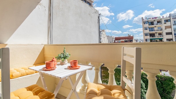 A balcony with a white table, yellow cushions, and a potted plant.