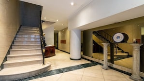 A grand staircase with marble steps and a black handrail, leading to a second-floor landing.