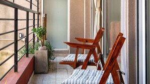 Un balcon avec deux chaises en bois, une plante en pot et une porte-fenêtre coulissante.