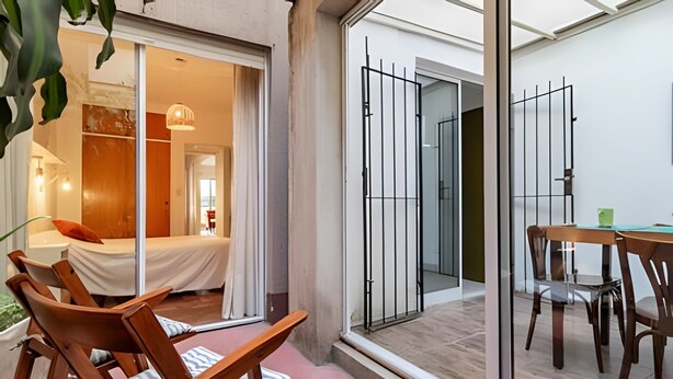 Une chambre d’hôtel moderne équipée d’un lit, de chaises en bois, d’une table à manger et d’une porte-fenêtre coulissante donnant sur un balcon.