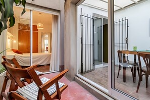 Ein modernes Hotelzimmer mit einem Bett, Holzstühlen, einem Esstisch und einer Glastür zum Balkon.