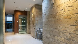 A modern hallway with stone walls, a glass elevator, and a seating area with chairs.