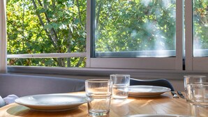 A dining table with plates, cutlery, and glasses, positioned near a window with a view of trees.