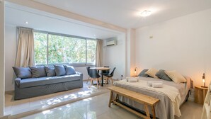 A modern, well-lit room with a sofa, a bed, a dining table, and a bench.