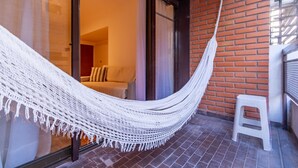 Eine Hängematte auf einem Balkon mit einer Ziegelwand und einer Glastür, die in einen Raum mit einer Couch und Kissen führt.