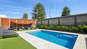 En swimmingpool med liggestole og en græsplæne.
