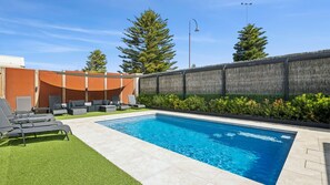 A swimming pool with lounge chairs and a grassy area. - Resort Living on Tempest (Torquay)