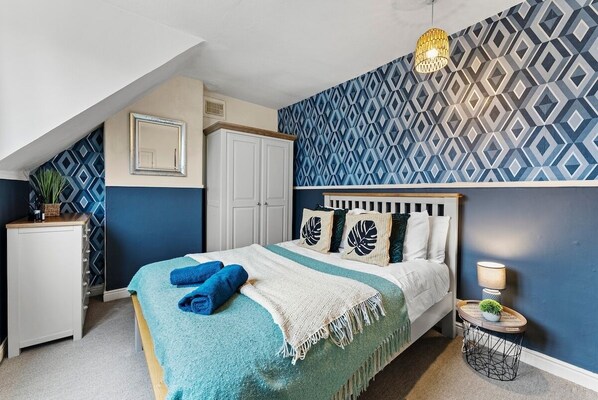 Un dormitorio con cama, mesita de noche, cómoda y pared con diseño.