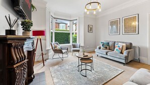 Ein Wohnzimmer mit einer Couch, Sesseln, einem Couchtisch, einem an der Wand befestigten Fernseher und einem großen Fenster.