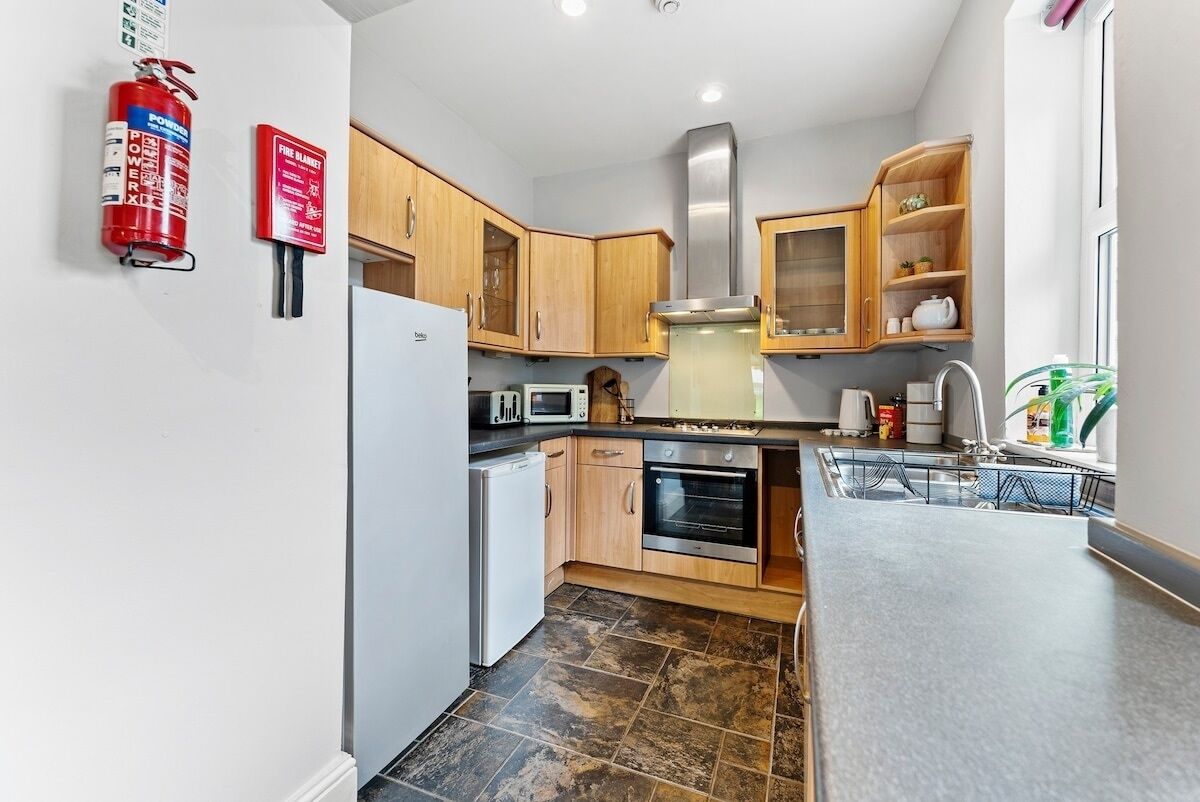 A compact kitchen with wooden cabinets, a stainless steel range hood, a built-in microwave, a white refrigerator, and a small oven.