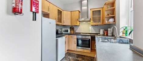 A compact kitchen with wooden cabinets, a stainless steel range hood, a built-in microwave, a white refrigerator, and a small oven.