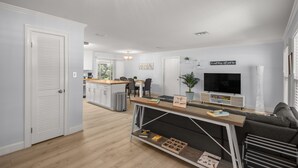 Un salon moderne avec un canapé, un téléviseur et une table basse. On aperçoit, au fond, un coin cuisine avec une table à manger et des chaises.