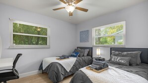 Une chambre avec deux lits, un ventilateur de plafond et de grandes fenêtres.