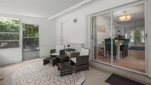 Une pièce meublée de mobilier en osier, une porte vitrée donnant sur un coin repas et un plafond blanc.