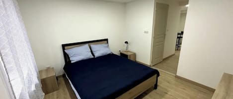 Un dormitorio con una cama de madera, paredes blancas y suelo de madera.