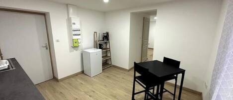 A small, open-plan living space with a kitchenette, a dining area with a table and chairs, and a built-in shelving unit.