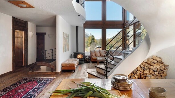 A modern interior with a spiral staircase, wooden flooring, and a large window offering a view of the outdoors.