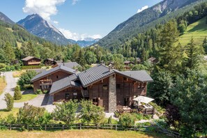 A mountain lodge with a stone chimney, wooden exterior, and a patio with outdoor seating.