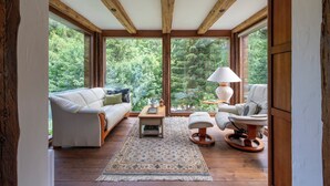 A spacious room with wooden beams, a white sofa, a chair, a small table, and a lamp.