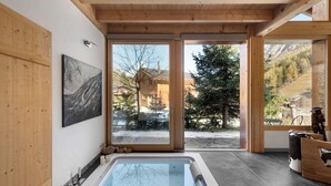 A modern bathroom with a large bathtub, wooden walls, and large windows offering a view of a snowy mountain landscape.