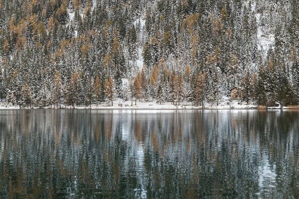 Un paisaje invernal sereno con un lago cubierto de nieve y árboles reflejados en el agua.