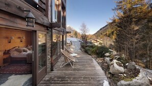 A wooden deck with chairs, a stone wall, and a view of a mountainous landscape.