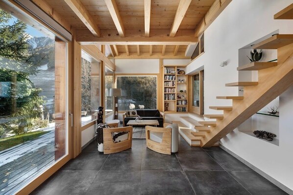 A modern interior with a wooden staircase, a black sofa, and a bookshelf.