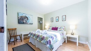 A bedroom with a bed, a chair, a bedside table, a lamp, and a painting on the wall. - Jellybean Dream upstairs apt: driveway, 4 bedrooms & near Bannerman Park! (St. John's)