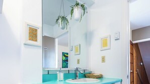 A bathroom with a white sink, turquoise countertop, and white cabinets. There are hanging plants above the mirror and a framed picture on the wall. - Jellybean Dream upstairs apt: driveway, 4 bedrooms & near Bannerman Park! (St. John's)