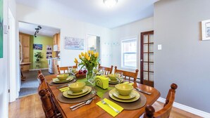 A dining area with a wooden table set for four, surrounded by chairs. There is a vase with yellow flowers on the table, and a map is visible on the wall. - Jellybean Dream upstairs apt: driveway, 4 bedrooms & near Bannerman Park! (St. John's)