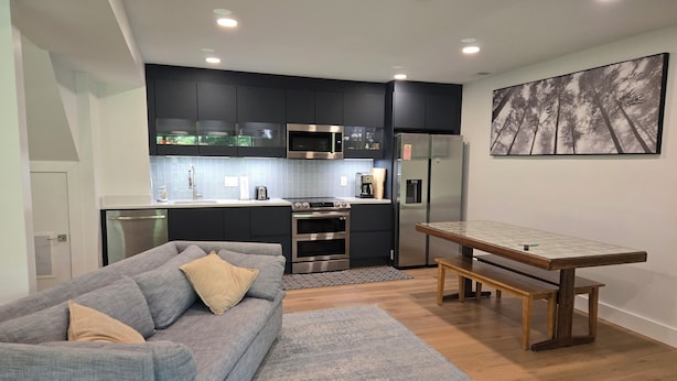 A modern kitchen with dark cabinets, stainless steel appliances, and a dining area with a wooden table and bench. - The Wooded Retreat (McLean)