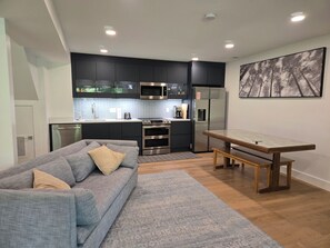 A modern kitchen with dark cabinets, stainless steel appliances, and a dining area with a wooden table and bench.
