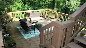 A wooden deck with outdoor furniture, including a sofa and chairs, surrounded by potted plants and flowers. - The Wooded Retreat (McLean)