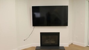 A room with a flat-screen TV mounted on the wall above a fireplace. - The Wooded Retreat (McLean)